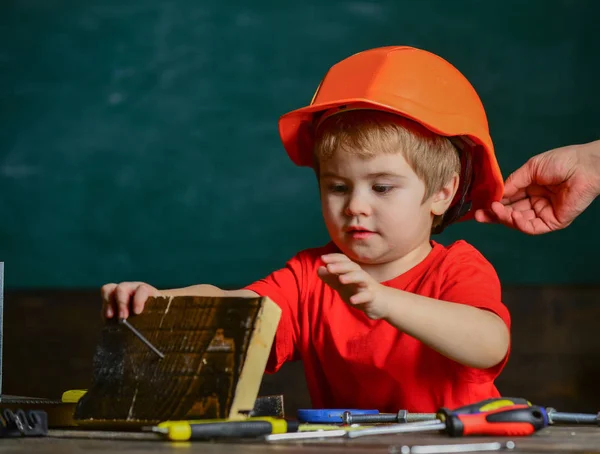 Protection and safety concept. Carefully protect kid with helmet. Toddler in protective helmet at workshop. Child cute and adorable play with wood and screw while male hand putting hard hat on head. — Stock Photo, Image