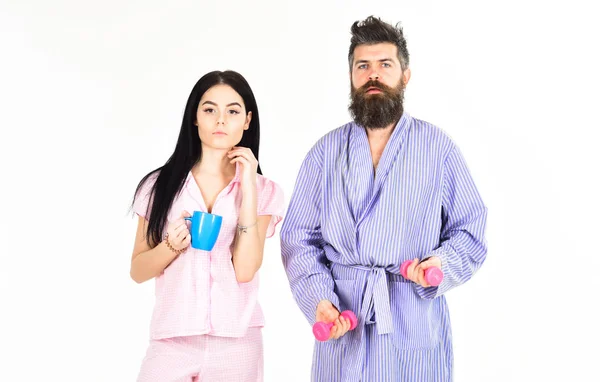 Couple, la famille offre une source d'énergie alternative. Couple amoureux en pyjama, peignoir isolé sur fond blanc. Homme avec haltère, fille avec tasse de café. Concept de mode de vie alternatif . — Photo