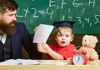 Baba, evde ile tek tek çocuk mutlu çalışmalar. Bireysel eğitim kavramı. Küçük çocuk onun defterini boya ile gösterir. Öğretmen ve öğrenci kolej, kara tahta arka plan içinde