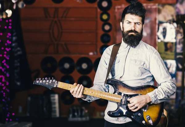 Talented musician, soloist, singer play guitar in music club on background. Musician with beard play electric guitar. Rock music concept. Man with strict face play guitar, singing song, play music