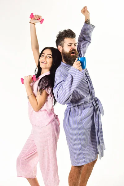 Couple, family on sleepy faces, stretching. Couple in love in pajama, bathrobe stand back to back. Girl with dumbbell, man with coffee cup, isolated on white background. Morning routine concept