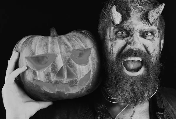Diablo o monstruo con decoraciones de octubre. El hombre que usa maquillaje aterrador sostiene la calabaza sobre el fondo negro . — Foto de Stock