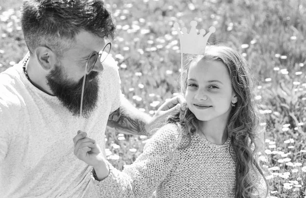 Concepto de mejores amigos. Papá y su hija se sientan en la hierba en Grassplot, fondo verde. Familia pasar el ocio al aire libre. Niño y padre posando con atributos de cabina de fotos de corona y anteojos — Foto de Stock