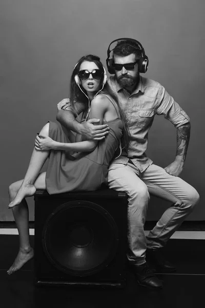 Technologies and music concept. Couple in love sits on black loudspeaker on red background