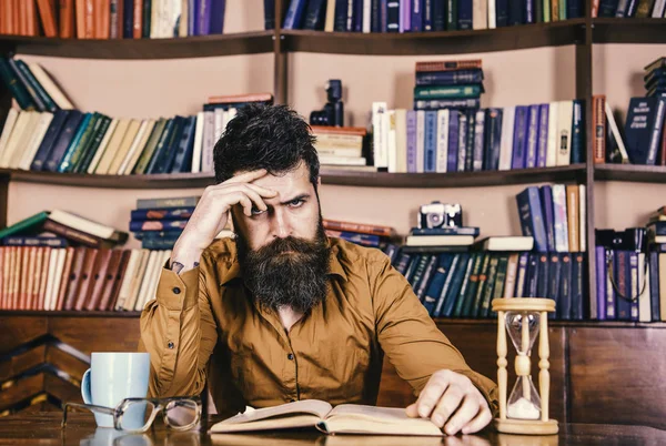 Öğretmen ya da sakal Kitaplığı'nda eğitim ile öğrenci. Eğitim, kitap rafı arka plan üzerinde konsantre yüz kitap, okuma kişi. Kendi eğitim kavramı. Kupa ve kum saati ile adam masada oturur