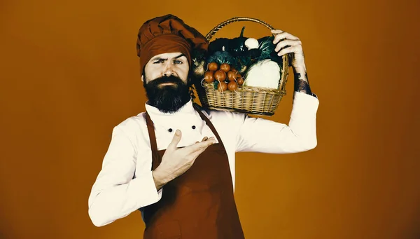 Chef-kok houdt kool, radijs, broccoli met sla en knoflook. Groene supermarkt concept. Man met baard op rode achtergrond — Stockfoto