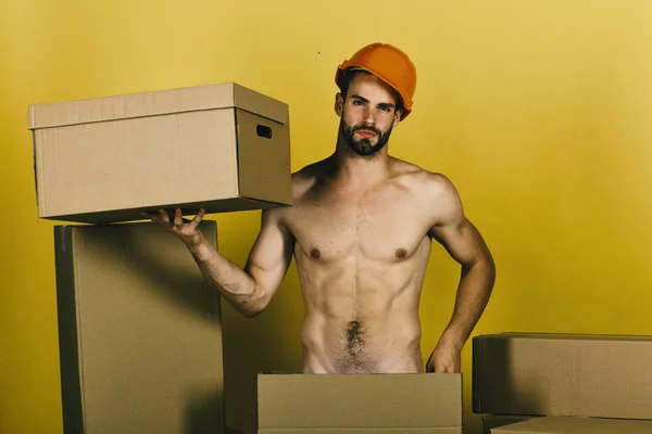 Tipo con torso sexy sosteniendo cartón sobre fondo amarillo. Hombre parado entre cajas de cartón como concepto de sexualidad y construcción — Foto de Stock