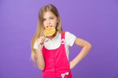Çocuk menekşe arka plan üzerinde lolipop yemek. Girdap karamel ile küçük kız. Mor zemin üzerine Stick şeker yiyor çocuk. Yemek ve tatlı. Beslenme ve diyet. Nefis öpücük