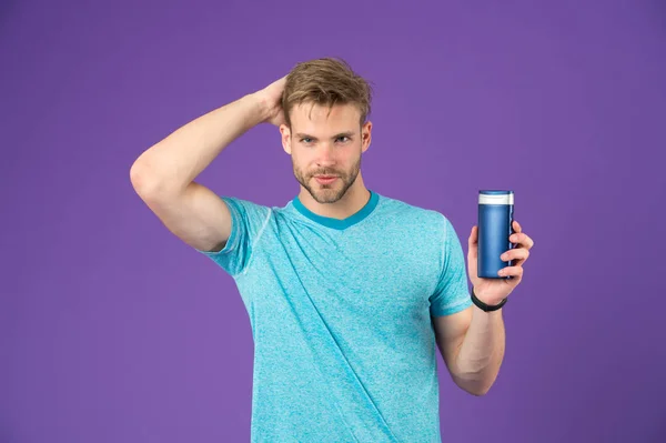 Hombre guapo con cuerpo sexy aislado sobre fondo púrpura. Modelo con cabello saludable celebración botella de champú, el cuidado del cuerpo y el concepto de cosméticos. Hombre con barba recortada acariciando su cabeza, mano en pelo — Foto de Stock