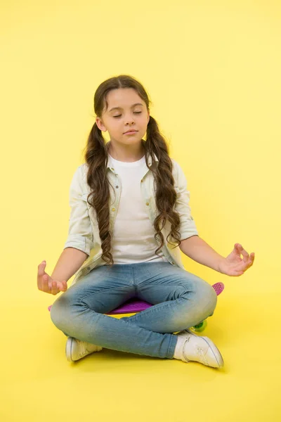 Chica meditar sentado en penny board sobre fondo amarillo. Niño pequeño relajarse en el monopatín. Hora del yoga. Concentración y meditación. Vive en paz y patineta — Foto de Stock