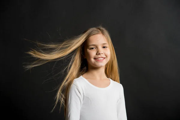 Μικρό κορίτσι χαμόγελο με μακριά ξανθά μαλλιά σε μαύρο φόντο. Ευτυχισμένο παιδί με μόδα hairstyle. Ομορφιά παιδί χαμογελώντας με αξιολάτρευτο βλέμμα. Σαλόνι ομορφιάς. Σε αυτό το σαλόνι αγαπάμε μαλλιά — Φωτογραφία Αρχείου