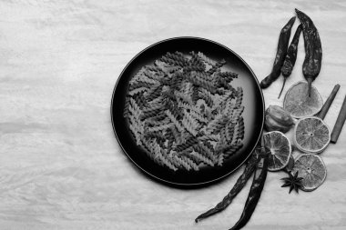 Lezzetli İtalyan makarnası seramik siyah tabak biber, portakal, sarımsak, yıldız anason ve tarçın, gri desenli arka plan, kopyalama alanı