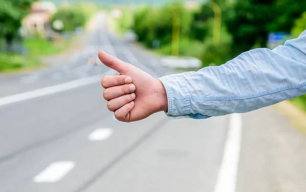 Most popular way of hitchhiking is to thumb up. Hand thumb up gesture try stop car road background. Thumb or hand gesture hitchhiking. Make sure you know right gestures used locally to stop car — Stock Photo, Image