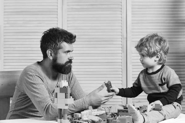 Dad and kid build of plastic blocks. Father and son with serious faces play with toy bricks