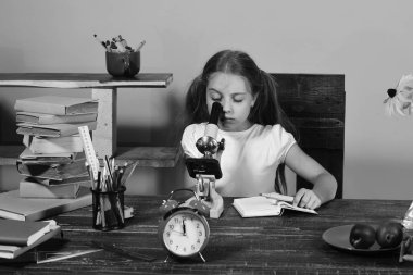 Pembe bir arka plan üzerinde çocuk ve okul malzemeleri. İleti örneği, saat, kitaplar ve çiçekler ile kız masa başında oturur