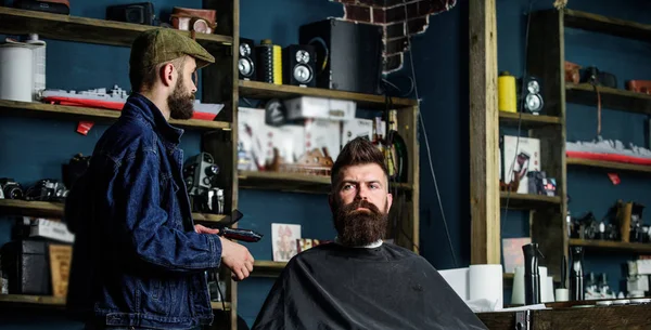 Hipster client got new haircut. Barber with hair clipper looking at mirror, barbershop background. Barber done haircut. Haircut concept. Professional master checking result while client sits in chair