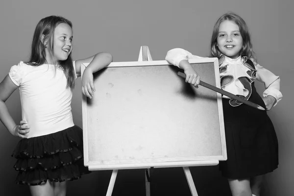 Chicas en uniforme escolar sobre fondo azul. Las colegialas con caras sonrientes sostienen un lápiz grande — Foto de Stock