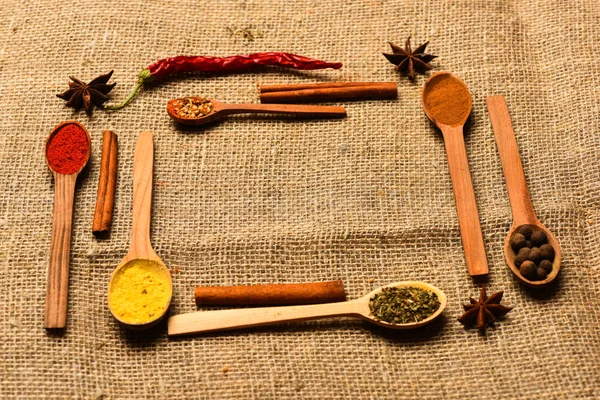 Condiments and spices concept. Spoons with spices as red pepper, curcuma and cinnamon on sackcloth background. Composition made out of spoons with spices. Spoons filled with kitchen herbs and spices