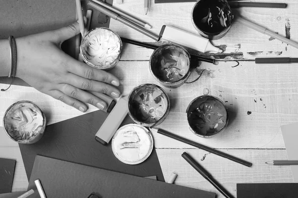 Art supplies near female hand on white wooden desk background, top view. Art and idea concept. Hand holds paint bowl by pencils and markers. Artists hand — Stock Photo, Image