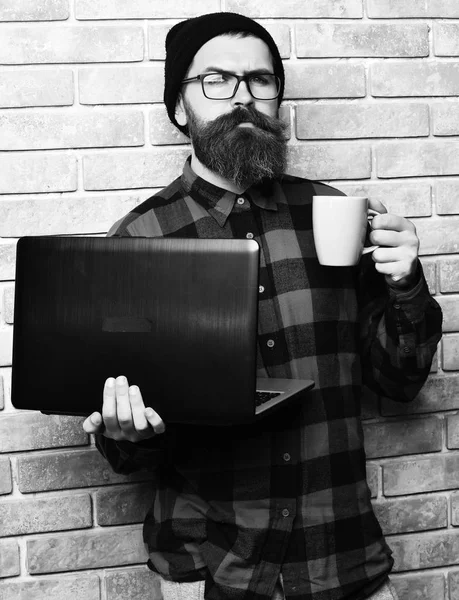 Bearded brutal caucasian hipster holding laptop with cup