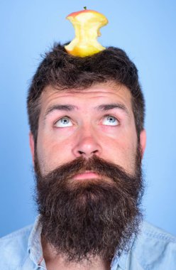 Canlı hedef kavramı. Adam yakışıklı hipster uzun sakal neredeyse kafasına elma güdük hedef olarak yem. Kilo kaybı gol. Hipster sürpriz yüz baş mavi arka plan üzerinde elma güdük hedefle yakın