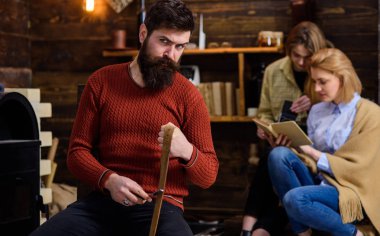 Oduncu ile sıkı bakmak ve uzun gür sakallı whetting jilet veya bıçak, tehlike kavram. Retro kıyafeti bıçak bileme sakallı adam. Eski ahşap evde kitap okurken chat yapan kızlar
