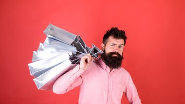 Sctrict yüzünde hipster bağımlısı alışveriş veya Alışverişkoliğin. Satış sezon indirimlerle alışveriş adam. Sakal ve bıyık taşır alışveriş torbaları omuz, kırmızı zemin üzerine olan adam. Alışveriş kavramı