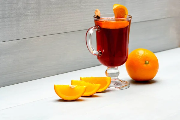 Glass with mulled wine or hot cider near juicy orange fruit on white wooden background. Drink or beverage with orange and cinnamon. Mulled wine near slices of orange. Cocktail and bar concept — Stock Photo, Image