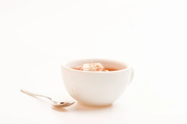 Tazza riempita con acqua calda e sacchetto intinto di tè nero. Processo di preparazione del tè nero in tazza di ceramica. Tazza riempita con acqua bollente, bustina di tè e cucchiaio su sfondo bianco. Concetto di tè — Foto Stock