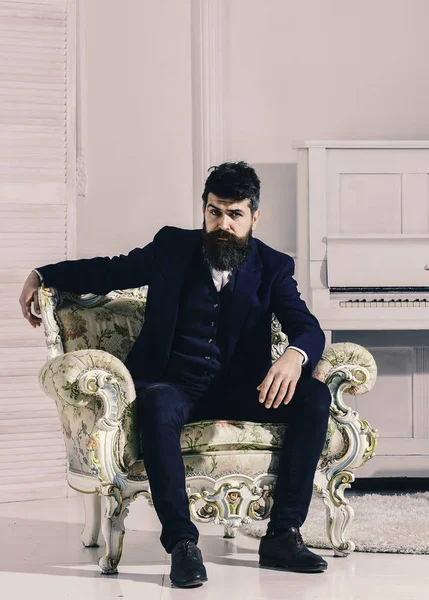 Concepto de riqueza y riqueza. Hombre con barba y bigote con traje clásico, elegante atuendo de moda. Macho atractivo y elegante en serio, cara pensativa sentado en un sillón a la antigua — Foto de Stock