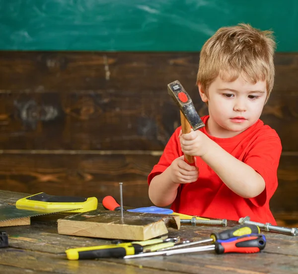 Child cute and adorable playing as builder or repairer, repairing or handcrafting. Handcrafting concept. Kid boy hammering nail into wooden board. Toddler on busy face plays at home in workshop — Stock Photo, Image