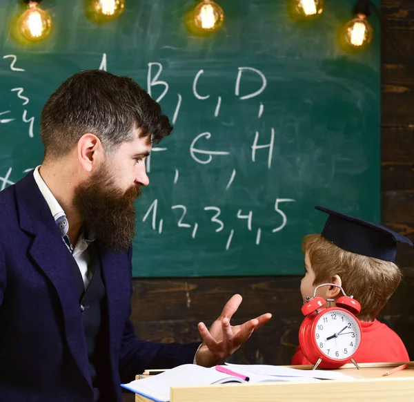 個人レッスンのコンセプトです。ひげの先生は、父は、教室の背景に黒板に幼い息子を教えています。少年は、大学院のキャップの子見て落書き黒板に先生が説明しながら — ストック写真