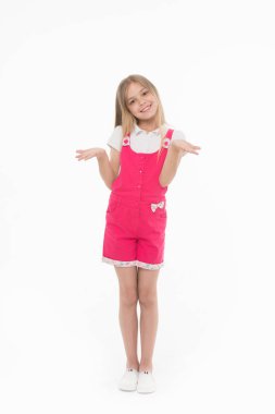 Girl in hot pink jumpsuit isolated on white background. Smiling kid wearing summer outfit. Child with hands in I dont know gesture. Blond girl with lovely face in studio, happy childhood concept