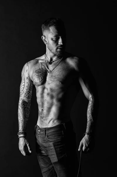 Sportsman or athlete in fashion jeans. Man with tattooed arm and chest. Bearded man with strong torso. Tattoo model with sexy belly. Bodycare with fitness and sport, black and white — Stock Photo, Image