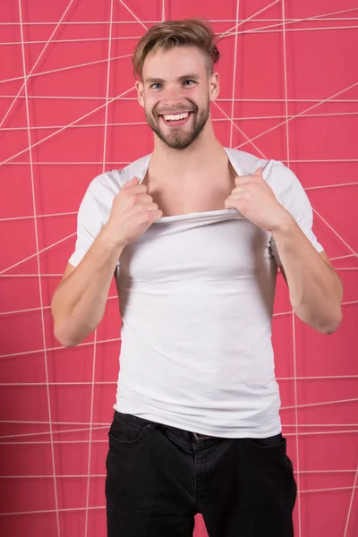 Tipo barbudo y atractivo arrancando la camisa. Hombre con cerdas en la cara feliz desvestirse, fondo rosa. Hombre con barba o sin afeitar chico se ve guapo y bien arreglado. Concepto de masculinidad — Foto de Stock