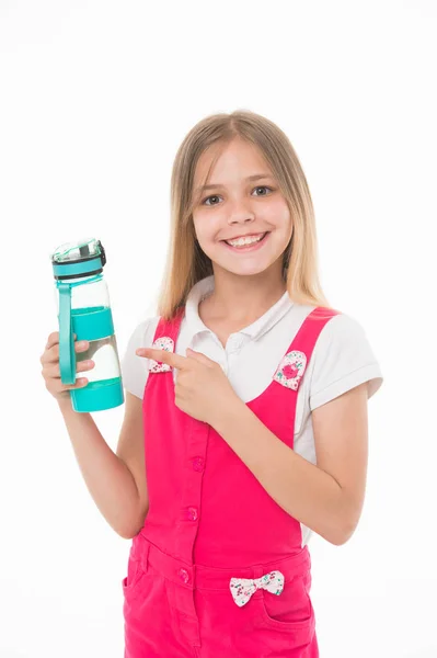 Une fille tenant une bouteille d'eau. Enfant avec un grand sourire portant une combinaison rose. Charmant enfant isolé sur fond blanc. Fille pointant vers bouteille en plastique bleu, habitudes saines, concept de nutrition — Photo