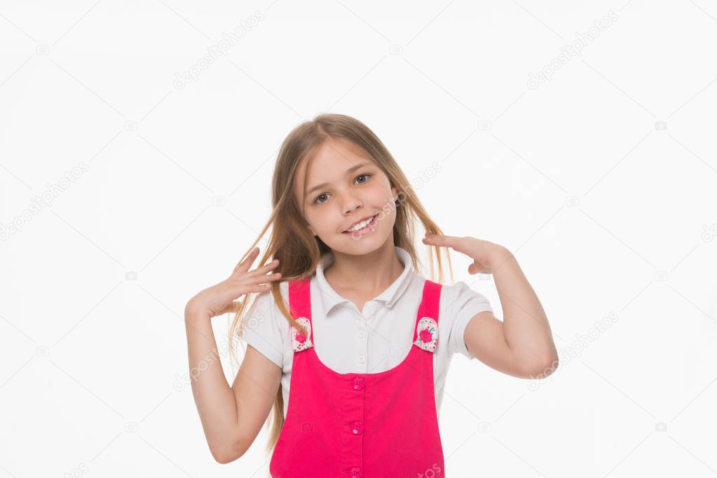 Girl stroking her long blond hair. Lovely kid with charming smile, beauty and childhood concept. Child in pink outfit isolated on white background. Playful girl with big hazel eyes posing in studio