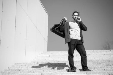 Adam mavi gökyüzündeki merdivenlerde cep telefonuyla konuşuyor.