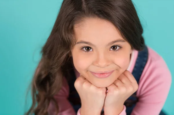 Cuteness överbelastning. Barn glada leende njuta av barndomen. Flicka bedårande leende glada ansikte lean på nävar avkopplande. Kid charmiga leende turkos bakgrund. Kid flicka långt lockigt hår söt glad — Stockfoto