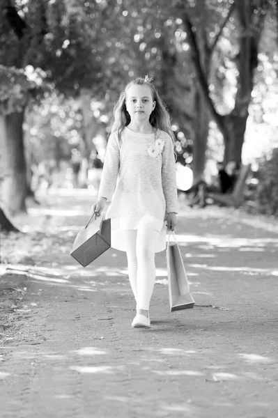 Criança com sacos de papel no verão. Menina com sacos de compras andar no parque. Pequena princesa com coroa no cabelo loiro longo. Kid shopper em roupas de moda ao ar livre. Compras à venda e compra — Fotografia de Stock