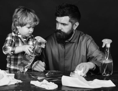 Küçük yardımcı kavramı anne. Lastik eldiven üzerinde temizlik malzemeleri ile masada sakallı adam. Şirin çocuk siyah adamla.