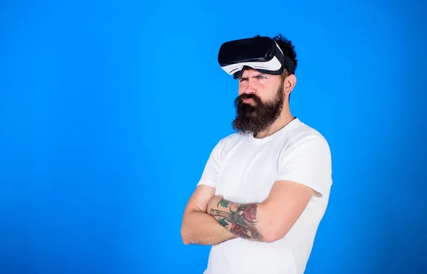 Man with long beard wearing VR headset over blue background. Bearded hipster with distrustful look ready to try new experience. Brutal macho with stylish beard skeptical about digital technologies