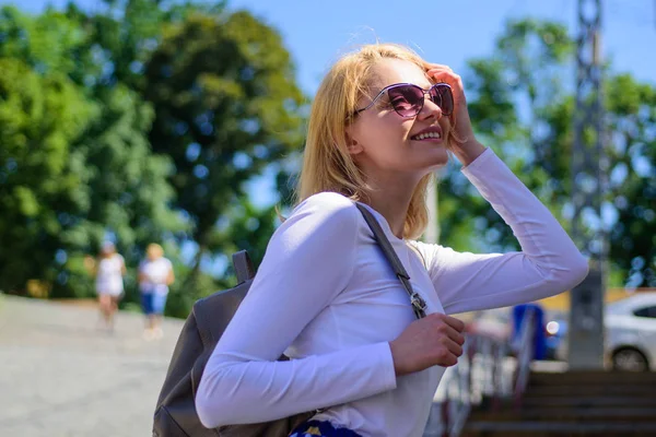 Женщина солнцезащитные очки наслаждаться прогулкой солнечный день, городской фон. Умный турист. Модная девчонка ходит. Женщина носит рюкзак, стоя на улице. Девушка со стильными прогулками — стоковое фото