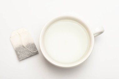 Kupa su ve çay poşeti beyaz zemin üzerine kaynar ile dolu. Çay zaman kavramı. Seramik Kupa, üstten görünüm demleme çay işlemidir. Şeffaf sıcak su ve çay torba ile fincan ya da beyaz Porselen Kupa