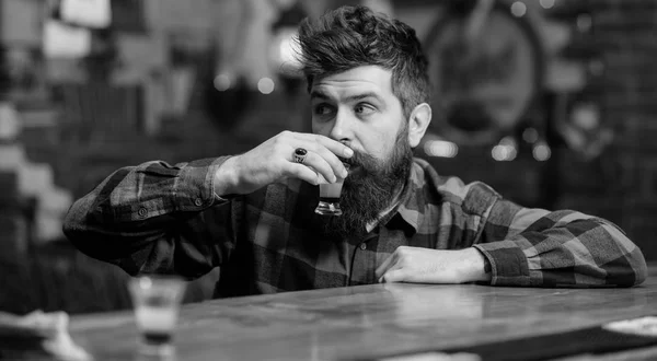 Depressed and sad man sit alone in bar or pub near bar counter. Hipster on thoughtful face drinks shot cocktail.