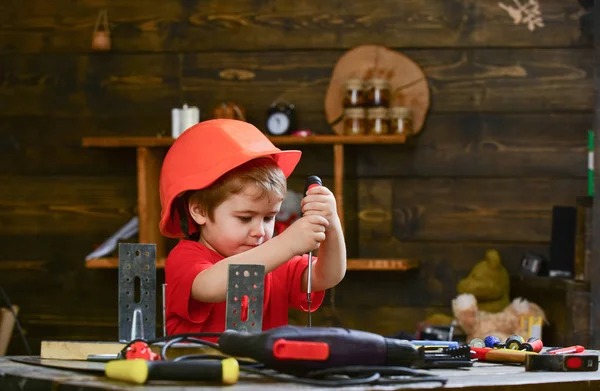 Concetto di infanzia. Ragazzo con cappello o casco arancio, sfondo della stanza di studio. Ragazzo giocare come costruttore o riparatore, lavorare con gli strumenti. Bambino che sogna una carriera futura in architettura o nell'edilizia — Foto Stock