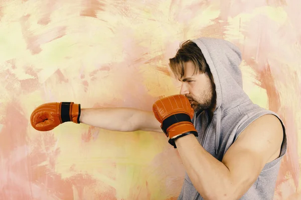 Man with messy hair on colorful background, copy space. Guy in grey sleeveless hoodie wears red leather boxing gloves Boxer with concentrated face trains and makes punch — Stock Photo, Image