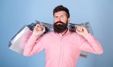 Adam serin öğeler, tatil acele kavramı aranıyor. Üzerinde mavi arka plan izole pembe gömlekli sakallı adam. Metroseksüel Gümüş Hediyelik çanta taşıyan kesilmiş sakallı. Sakallı adam alışveriş hakkında deli