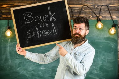 Gözlük öğretmen okul için başlıklı yazı tahtası tutar. Lise kavramı. Sakal ve bıyık katı yüz memnuniyetle öğrencilerin, kara tahta arka plan ile adam