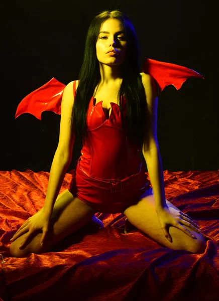 Sexy devil concept. Girl sexy demon with wings, devil full of desire. Woman on passionate face play role game. Lady sexi dressed as demon, devil, black background. Demon sexy girl sit on silk sheets — Stock Photo, Image